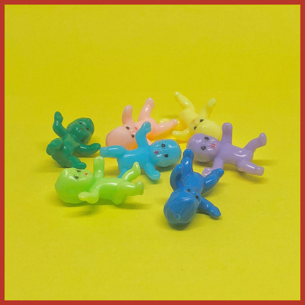 Image of seven miniature plastic babies on a yellow background. The babies are a different colour each; lime green, dark green, light blue, navy blue, purple, yellow and pastel pink.